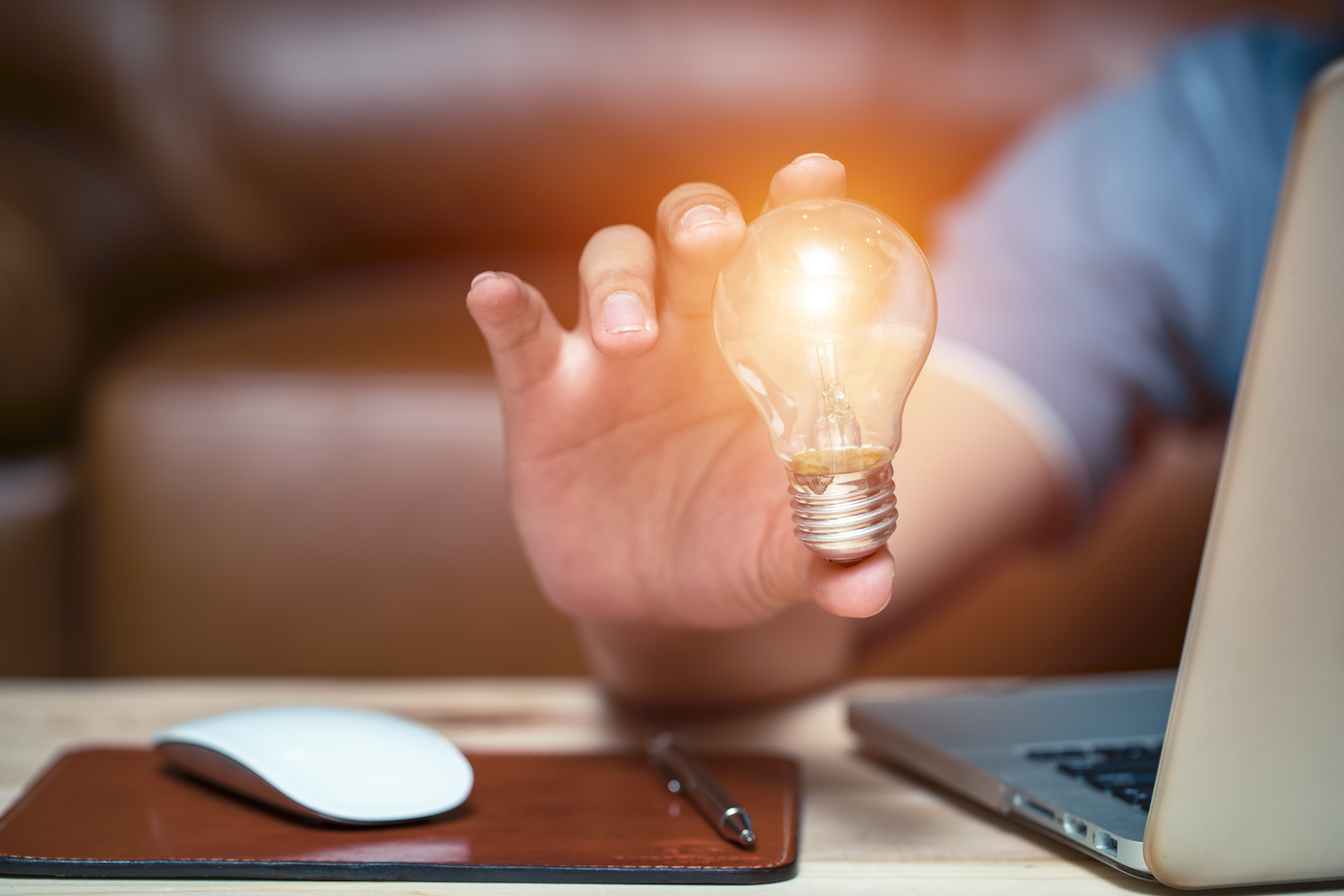 Someone sitting at a desk, holding a lightbulb that is illuminated apparently without a source of power.