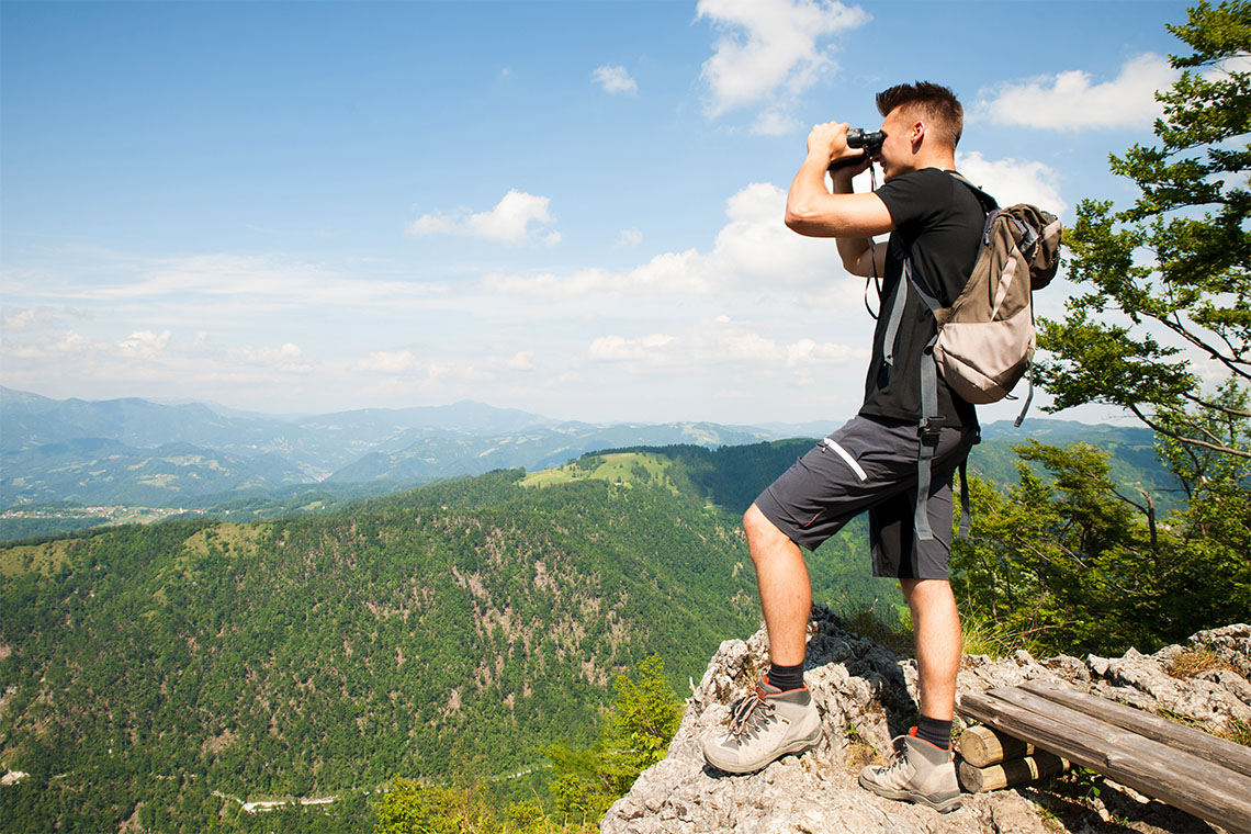 A silhouette of a man holding binoculars on a mountain top.