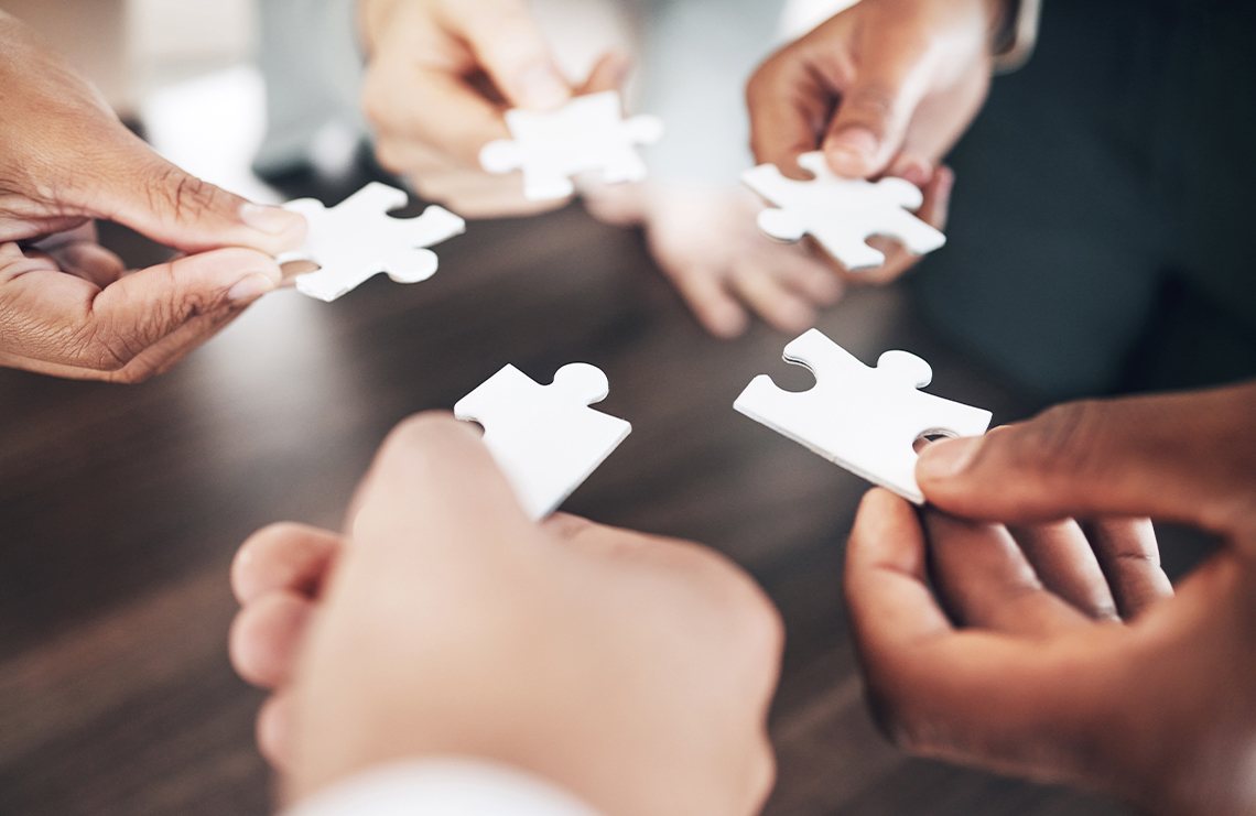 Many hands holding puzzle pieces close together.