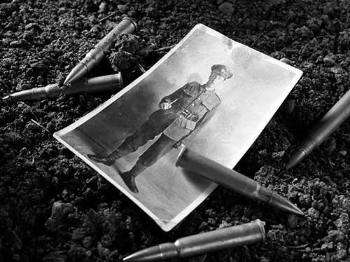 An old black and white photo of a soldier in WWI laying in the dirt with bullets around it