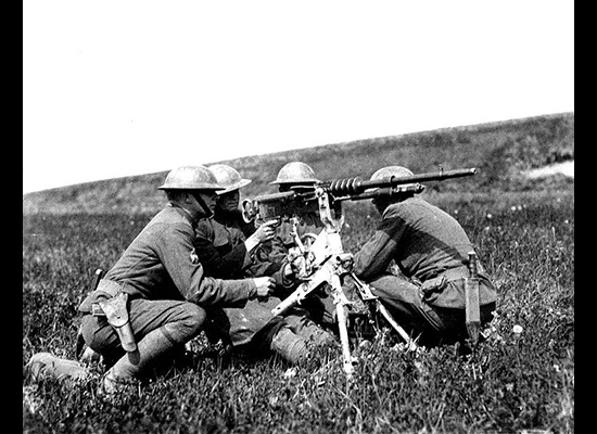 Four soldiers crouched around a machine gun on a three-legged stand in an empty field
