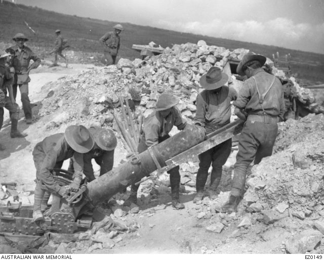 Soldiers load a large, six foot long gun that is planted in the trench and aimed at about a 30 degree angle.