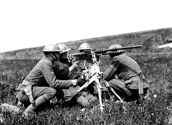 Four soldiers crouched around a machine gun on a three-legged stand in an empty field