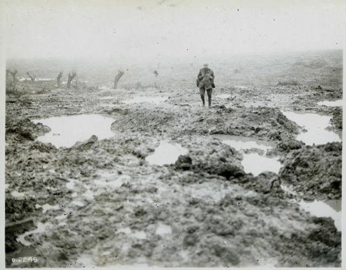 A soldier making his way across a field of mud.