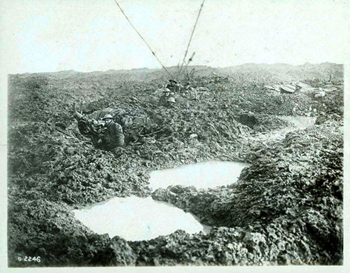 Soldiers crouching in mud holes beside puddles of water in fields of war.