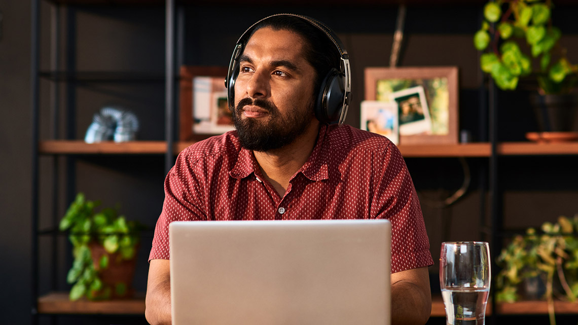 mid-adult man wearing headphones, using laptop, and looking away.