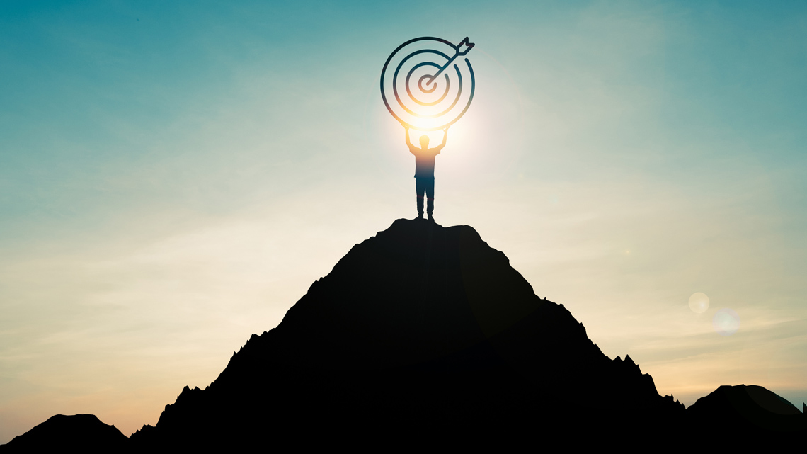 A person at the top of a mountain holding a target board.