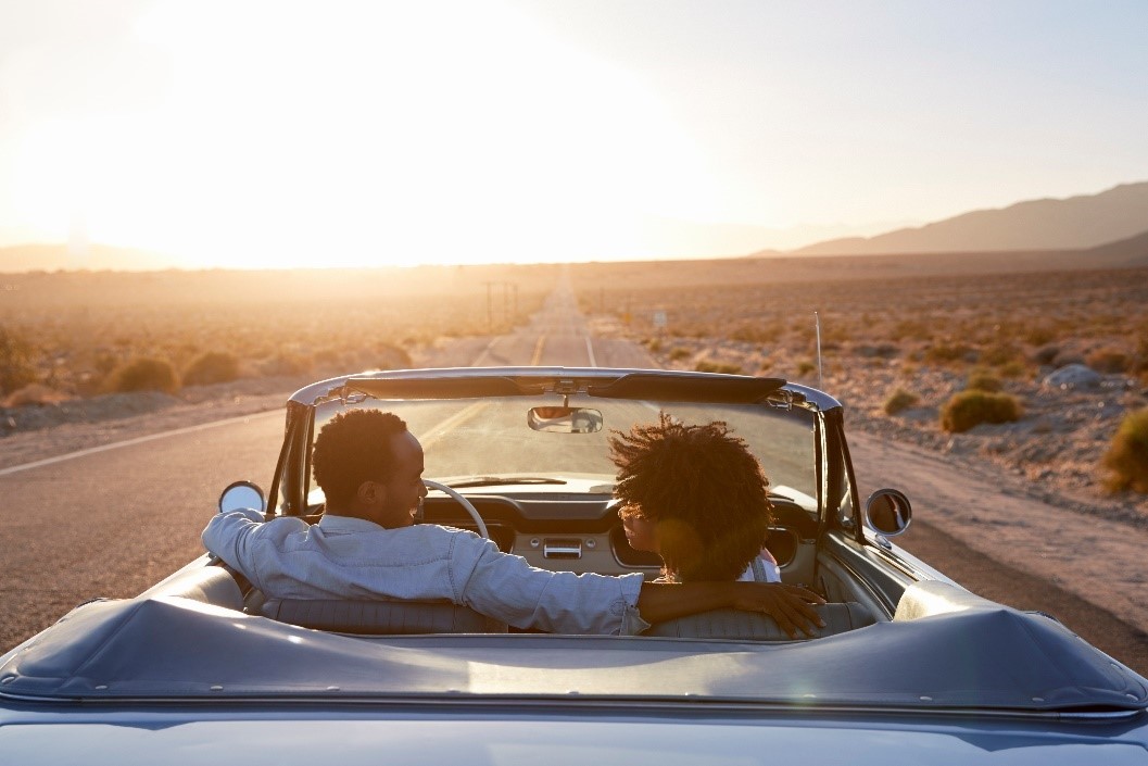 Un couple dans une voiture décapotable au coucher du soleil