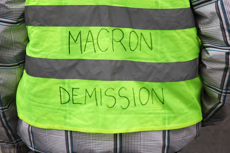 gilet rayé jaune et gris avec les mots “Démission Macron”