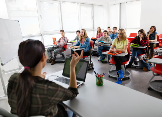 A teacher sitting and talking in front a class full of students.