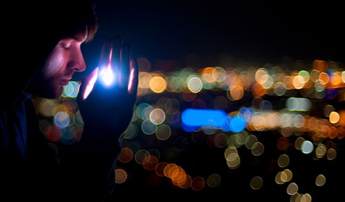 Young man praying at night, with city lights in the background.