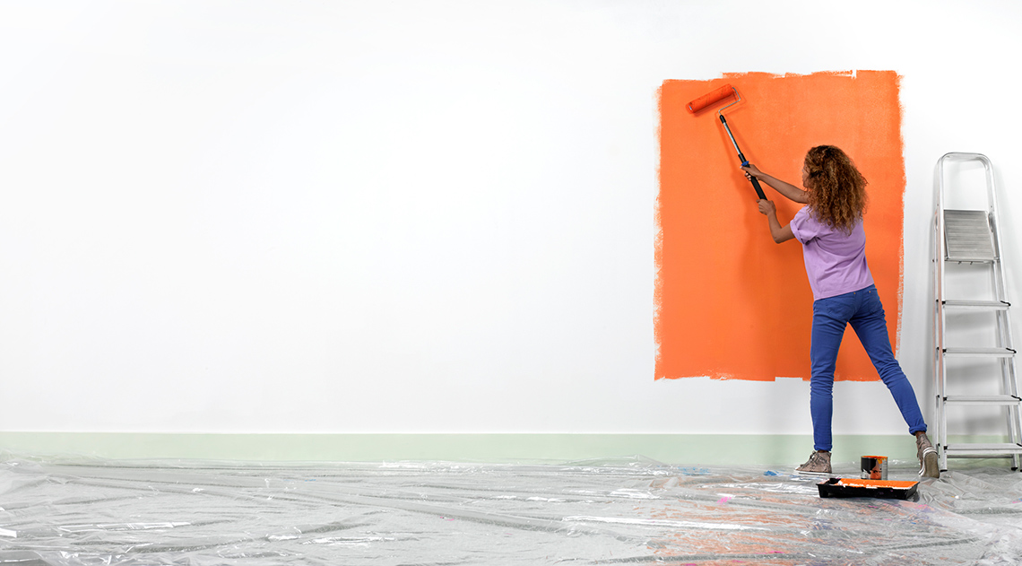 A person painting a wall with orange paint