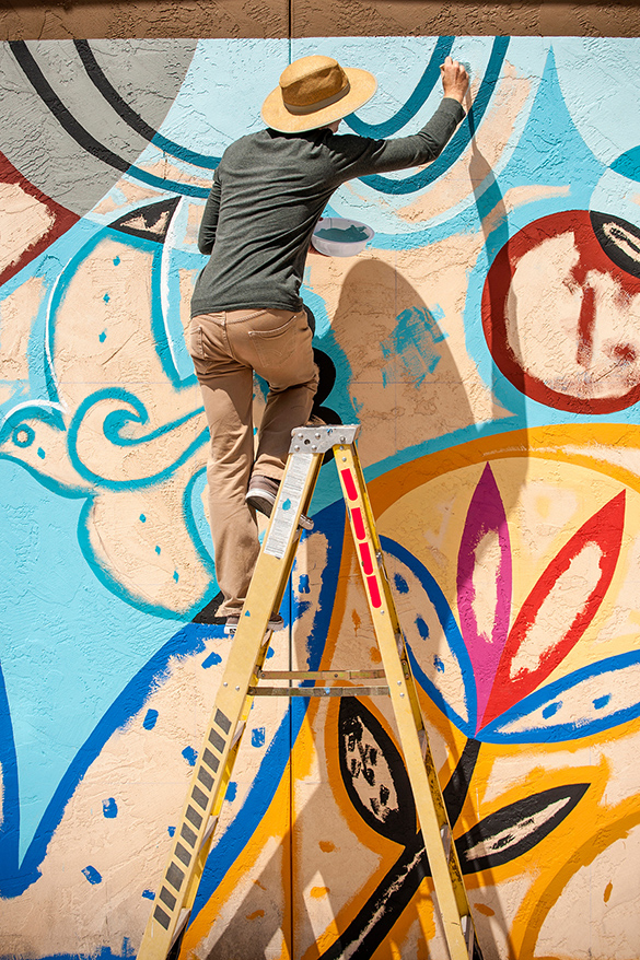 An artist painting a mural on a wall outdoors