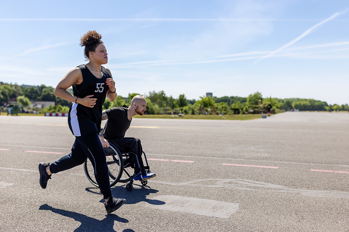 A person running beside a person in a wheelchair.