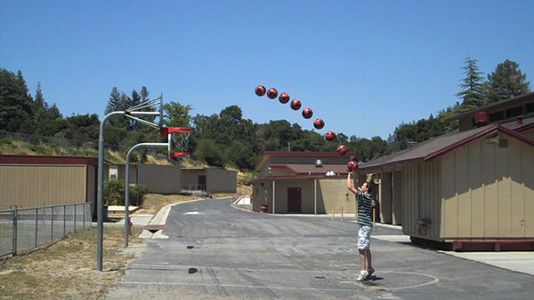 Child throwing a basketball. Depicts a single-curve trajectory of multiple basketballs. Basketball motion captured with multi-exposure photography.