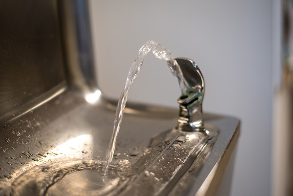 Stainless steel drinking water fountain making water flow in single arc-shaped stream.
