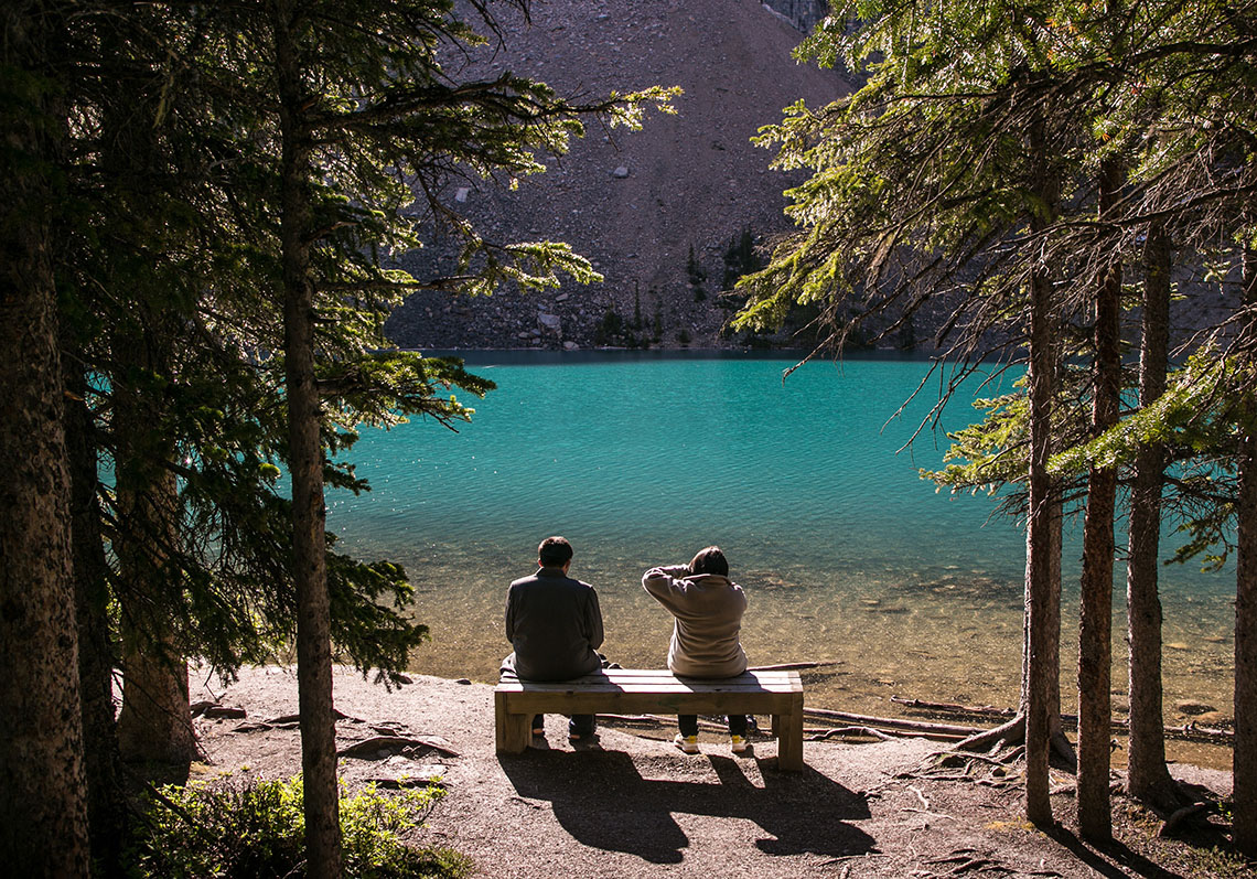 Two people sitting on a bench looking at Moraine Lake, Alberta, Canada
