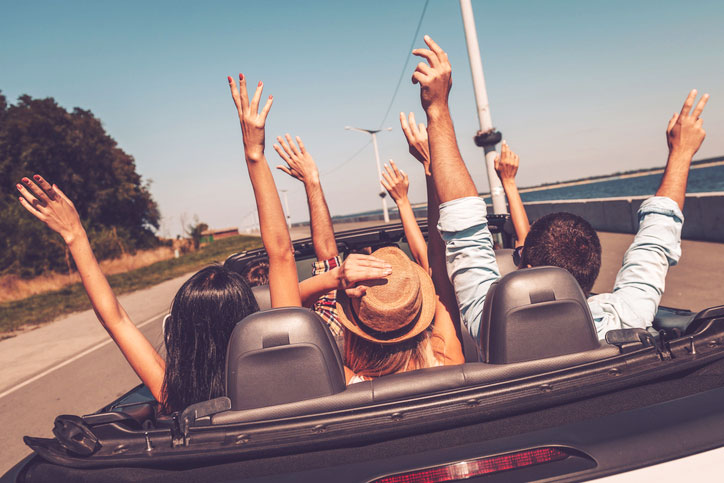 Rear view of young happy people enjoying road trip in their convertible and raising their arms up