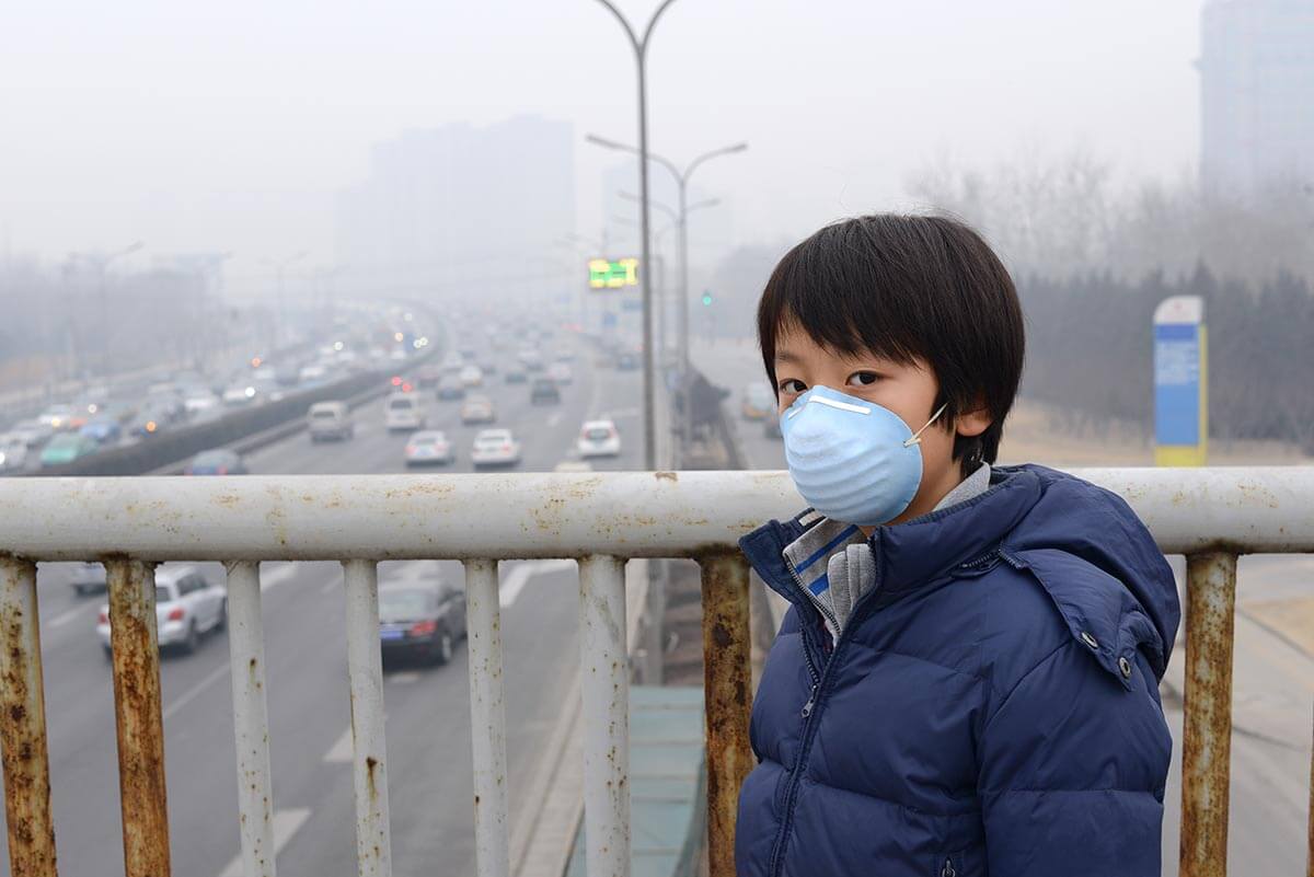 Child wearing a pollution mask on a foggy bridge.
