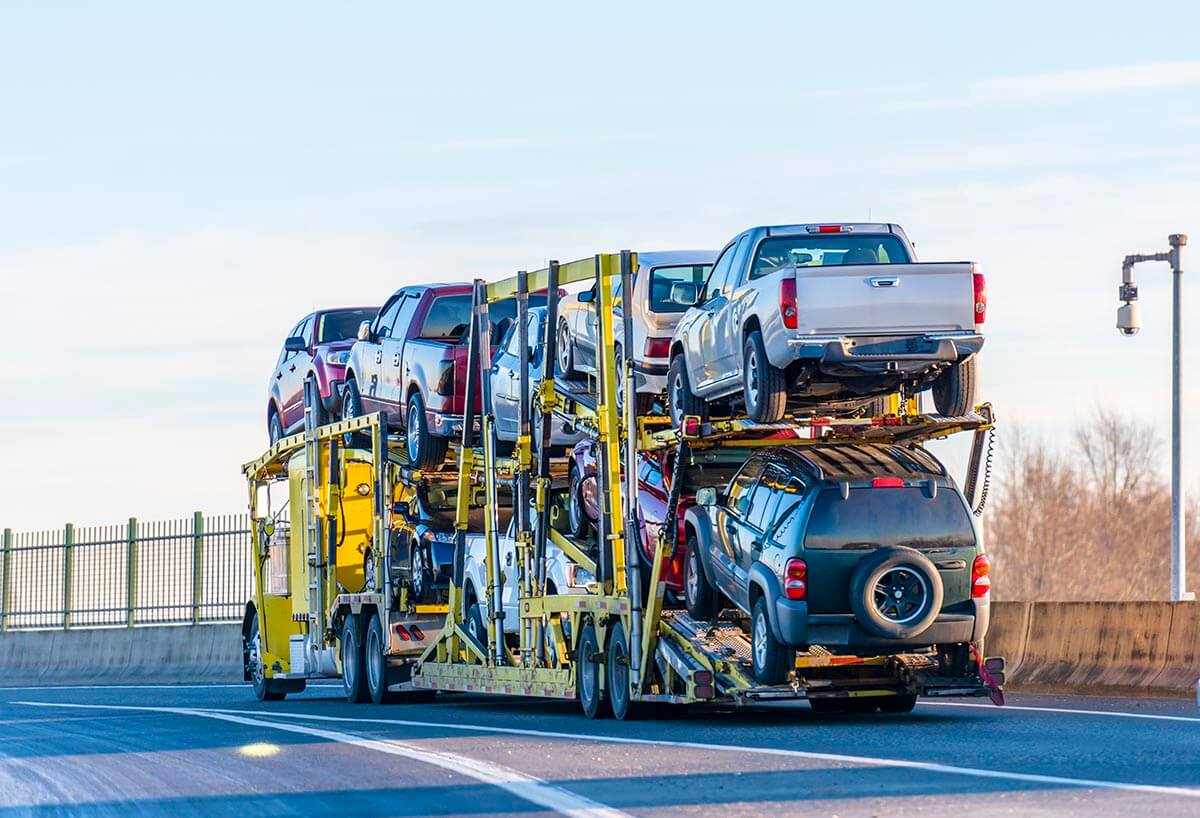 Big rig industrial grade yellow classic bonnet car hauler semi truck transporting cars on two levels semi trailer driving on the overpass road with protective fence on the side