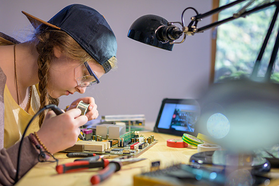 A teenager soldering a motherboard from a computer.